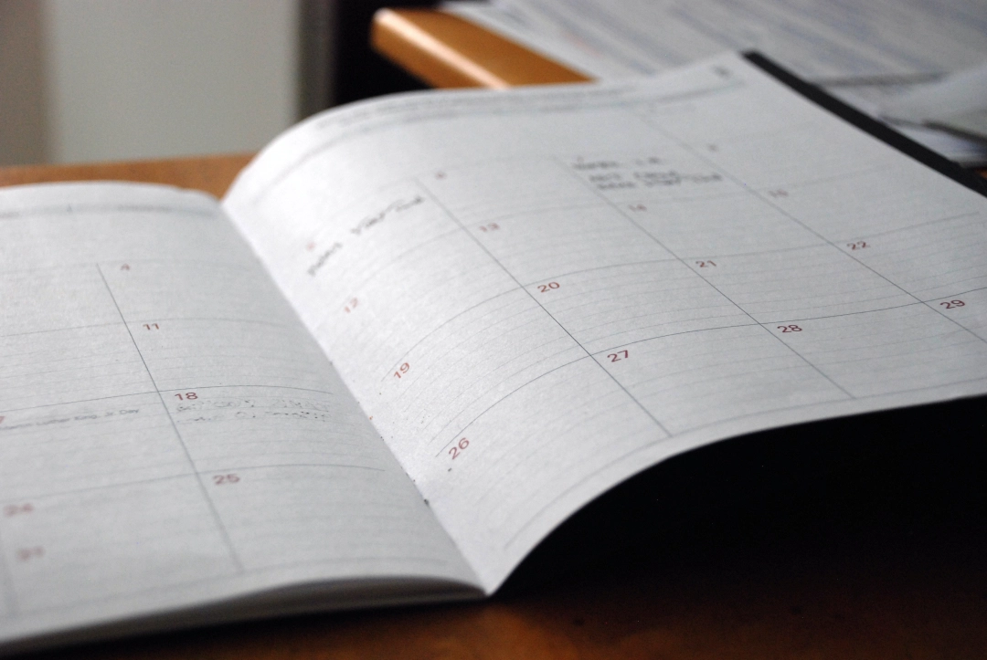 Otwarty papierowy kalendarz leży na biurku.