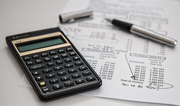 Kalkulator, długopis i dokumenty finansowe na białym stole.