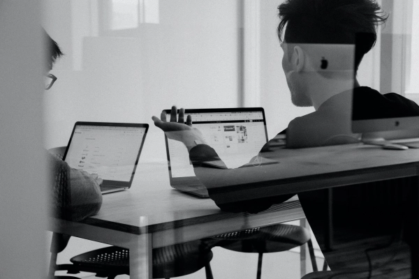 Dwóch mężczyzn pracujących przy laptopach, wymieniających się doświadczeniami.
